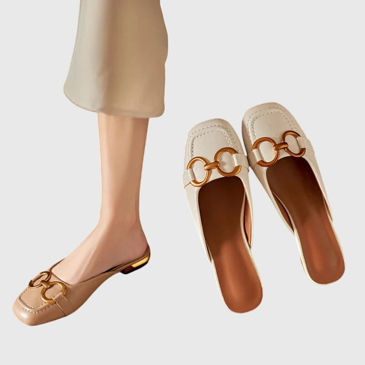 A cream closed-toe mule with a gold horsebit ring detail and a low heel.