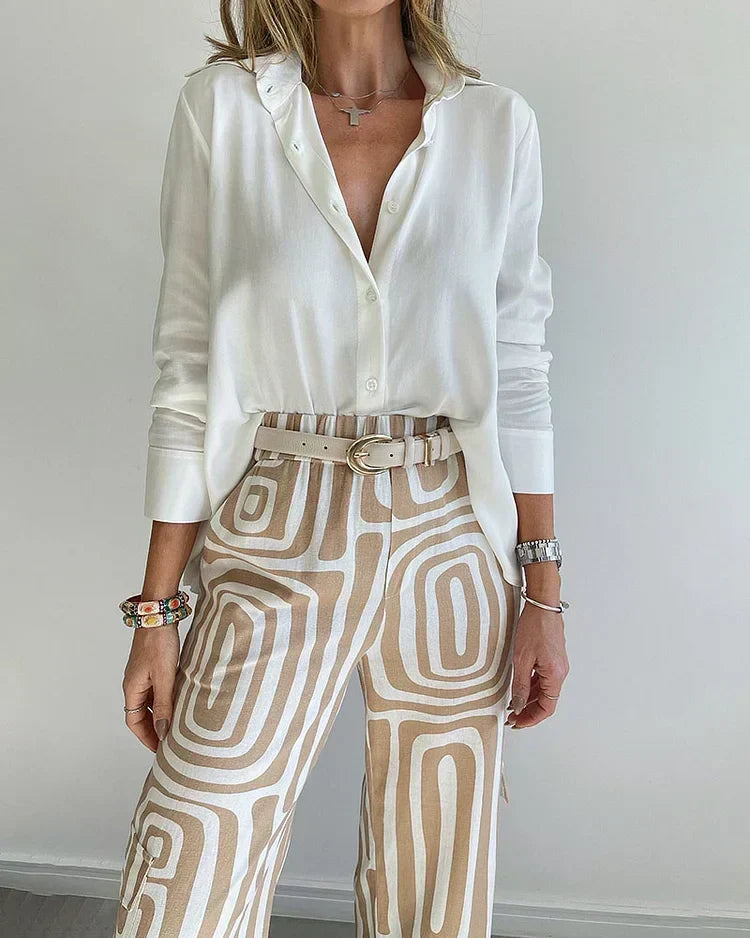 A woman wearing a plain button-up top with geometric-print pants and a belt at the waist.