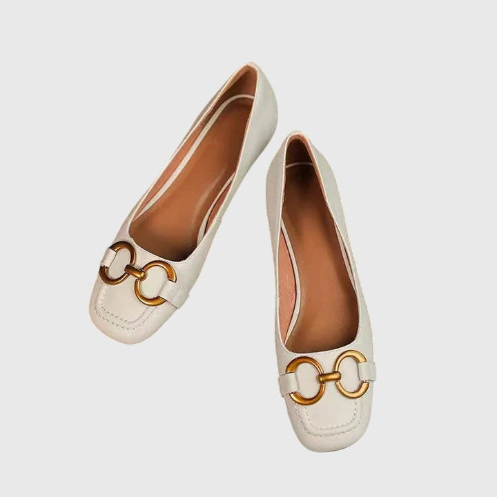 A pair of black slip-on flats with a polished gold ring detail across the toe.