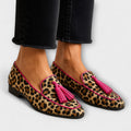 A woman wearing leopard-print loafers with pink tassels on a stylish day out.