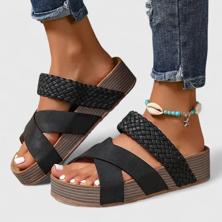 A woman strolling on a sunny street wearing beige woven comfort sandals with crossed straps.