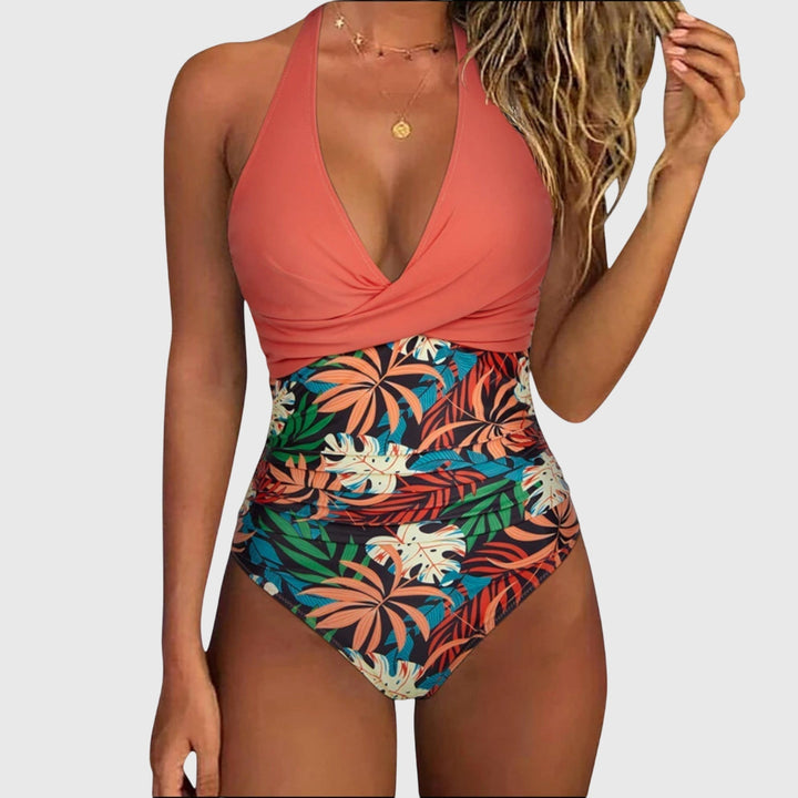 A woman by the sea in an elegant V-neck printed swimsuit, confident and relaxed in the sun.