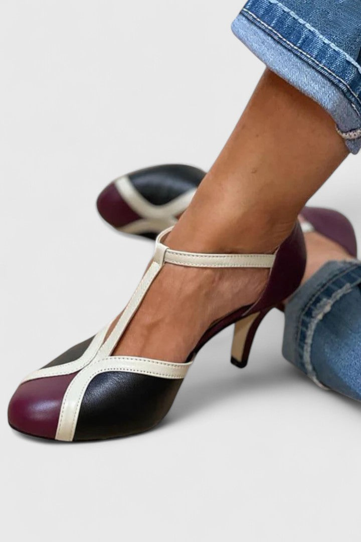 A woman wearing navy, blush and gold T-strap heels with a rounded toe, paired with jeans.