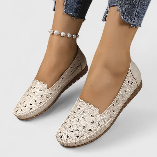 A woman wearing white floral cut-out slip-on flats on a warm, sunny day.