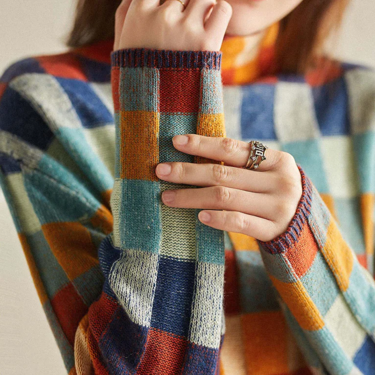 A woman wearing a colourful retro check sweater, relaxed and cosy on a cool fall morning.