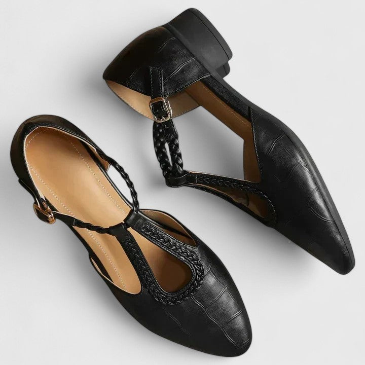 A woman wearing black pointed T-bar flats with a braided detail and ankle buckle.