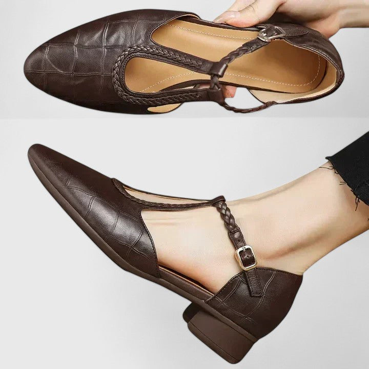 A woman wearing black pointed T-bar flats with a braided detail and ankle buckle.