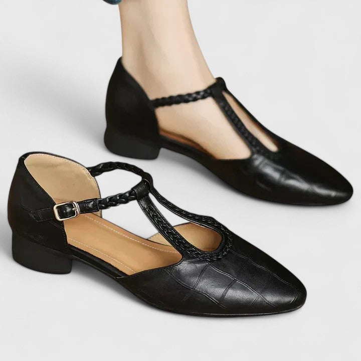 A woman wearing black pointed T-bar flats with a braided detail and ankle buckle.