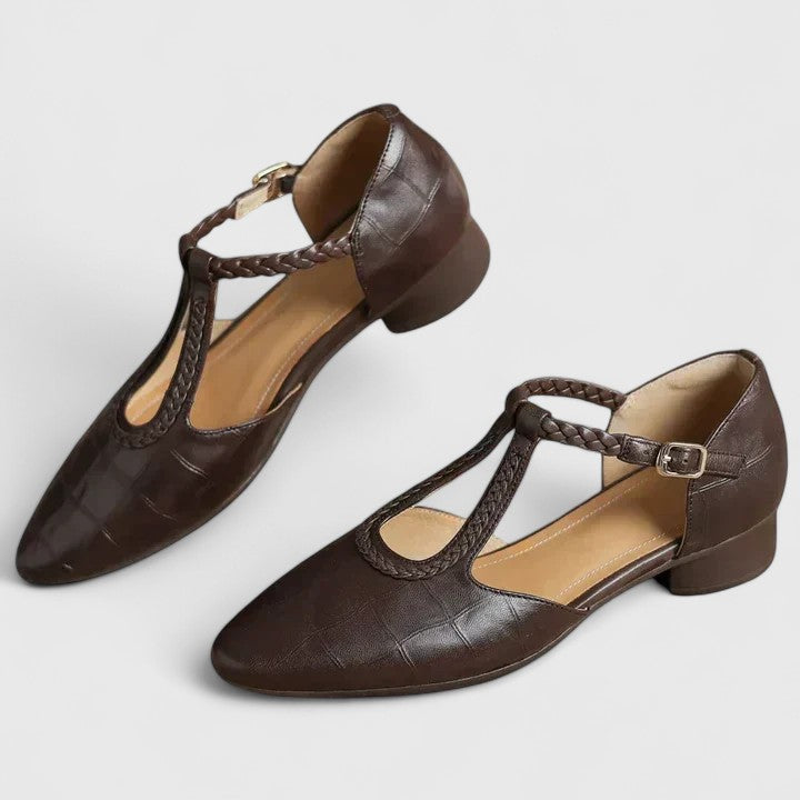 A woman wearing black pointed T-bar flats with a braided detail and ankle buckle.