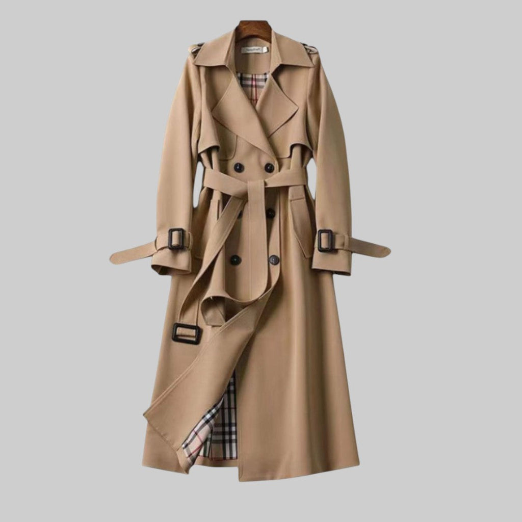 A woman wearing a belted classic trench coat with a defined waist, walking through the city.