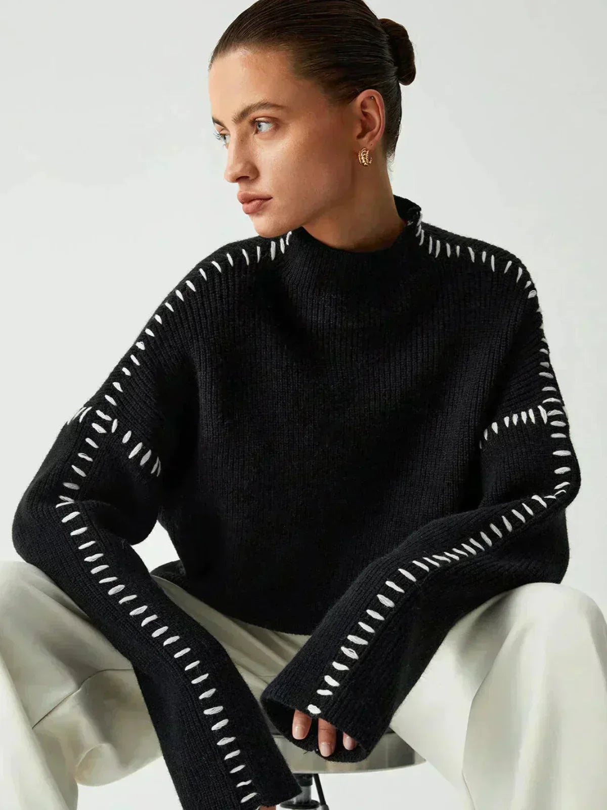 A woman wearing an oversized mock-neck sweater with whipstitch detailing, cosy and stylish.