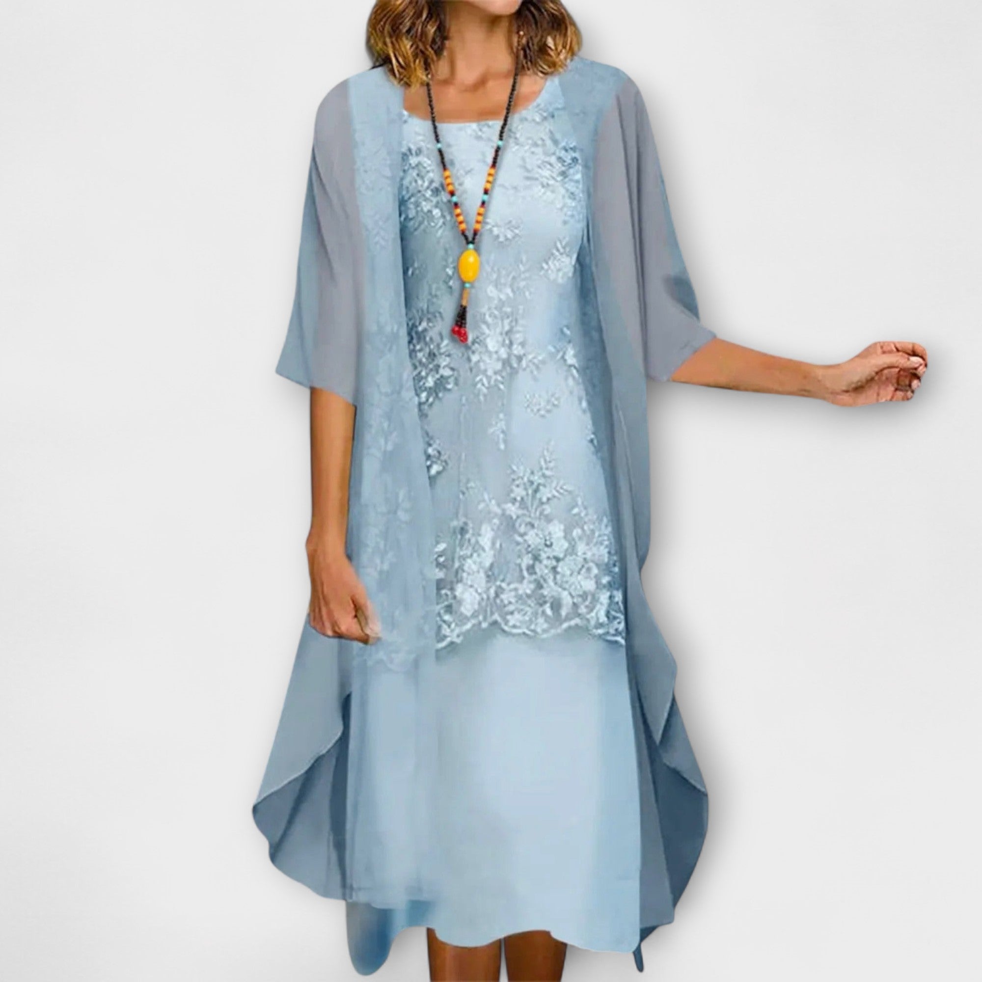 A woman wearing the Joanne layered dress in champagne, with floral embroidery, a square neckline and a sheer overlay.