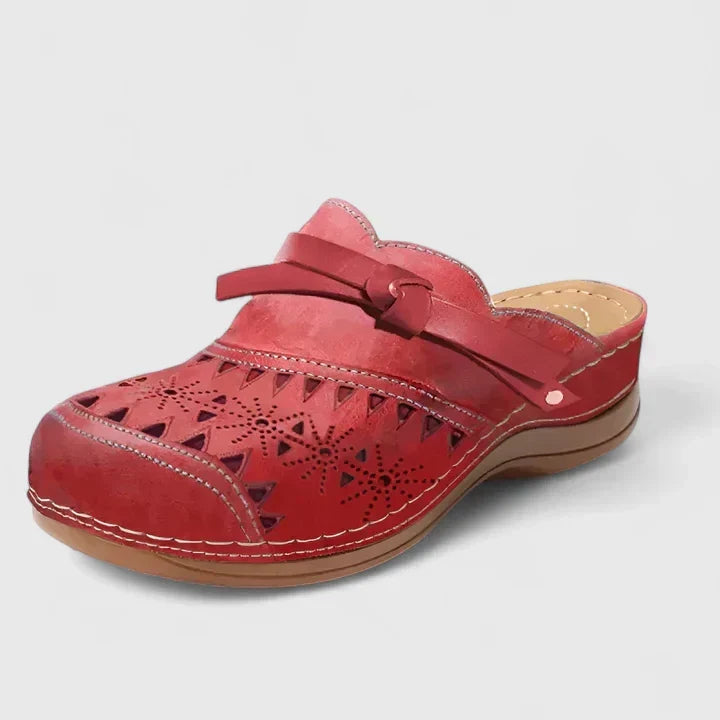 A woman slipping on airy laser-cut comfort shoes with a decorative knot detail at home.