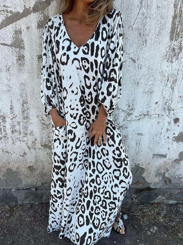 Woman in the Alison leopard print maxi dress with long sleeves and a V-neckline, walking along the shoreline.