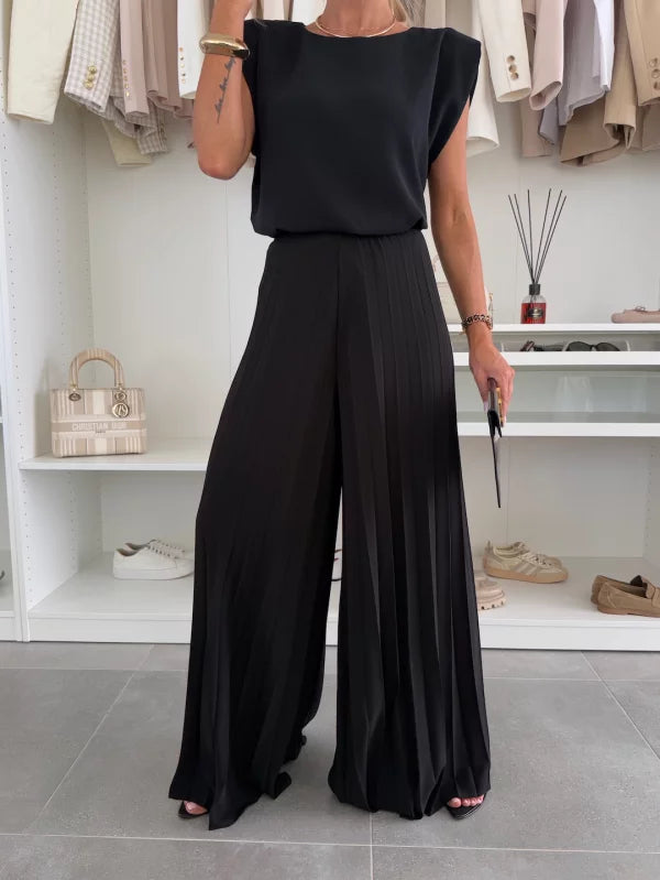A woman wearing a structured sleeveless top with high-waisted pleated wide-leg pants.