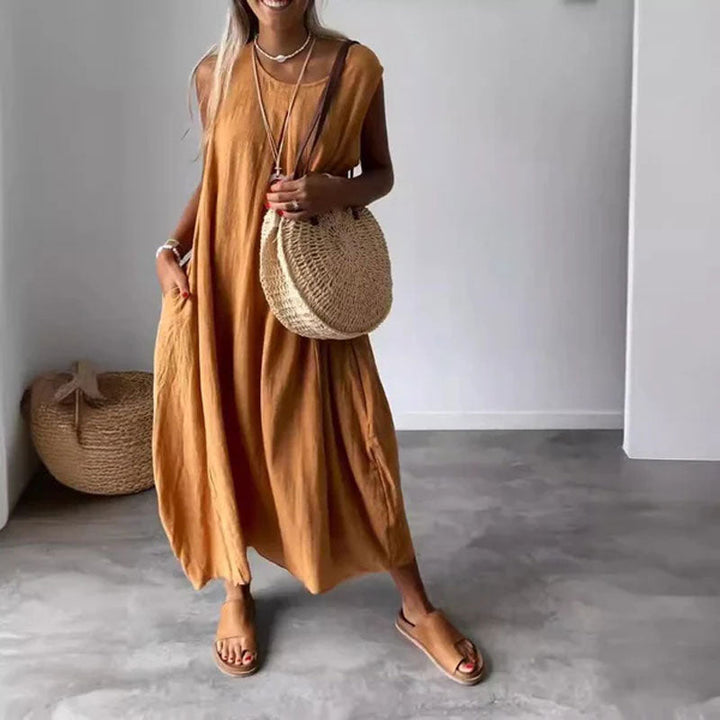 Woman wearing the Denise™ sleeveless flowing maxi dress with side pockets, relaxing outdoors on a warm day.