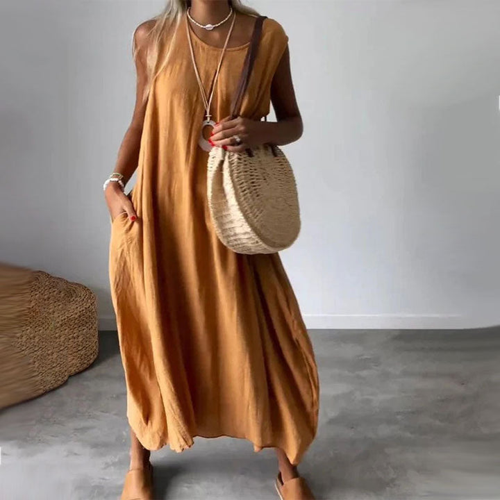 Woman wearing the Denise™ sleeveless flowing maxi dress with side pockets, relaxing outdoors on a warm day.
