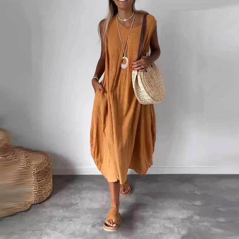Woman wearing the Denise™ sleeveless flowing maxi dress with side pockets, relaxing outdoors on a warm day.
