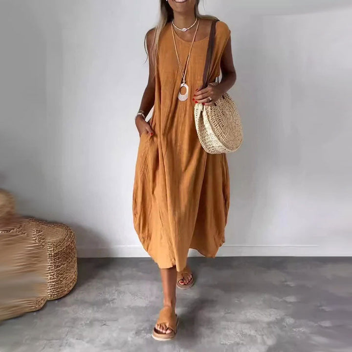 Woman wearing the Denise™ sleeveless flowing maxi dress with side pockets, relaxing outdoors on a warm day.