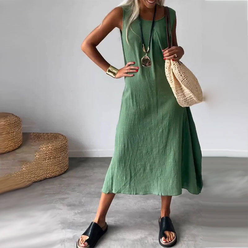 Woman wearing the Denise™ sleeveless flowing maxi dress with side pockets, relaxing outdoors on a warm day.