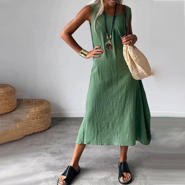 Woman wearing the Denise™ sleeveless flowing maxi dress with side pockets, relaxing outdoors on a warm day.