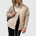 A woman wearing a light grey quilted jacket with chunky textured sleeves and a tall funnel collar.