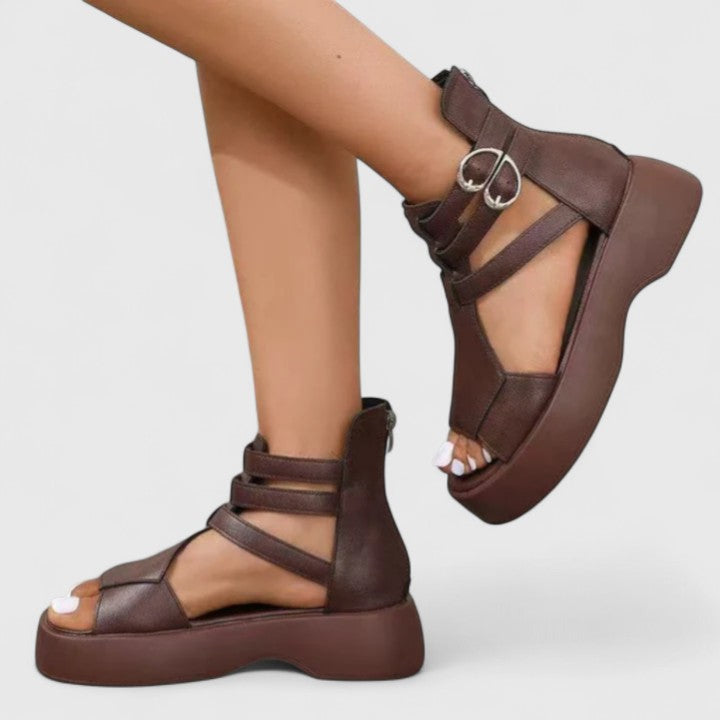 A woman stepping out in black platform sandals with crossover straps and a back zip, walking with a confident, easy stride.