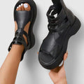 A woman stepping out in black platform sandals with crossover straps and a back zip, walking with a confident, easy stride.