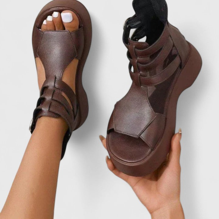 A woman stepping out in black platform sandals with crossover straps and a back zip, walking with a confident, easy stride.