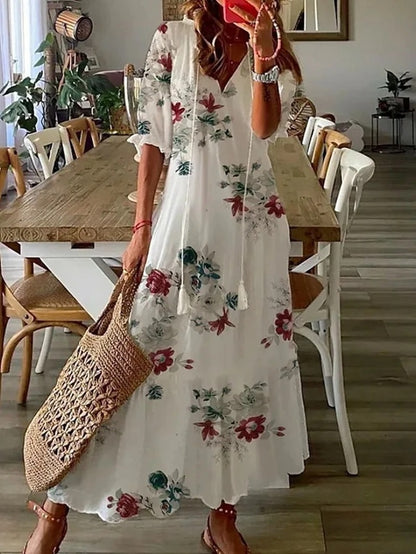 Woman wearing the Jacqueline™ boho maxi dress with fringe details and a V-neckline, relaxed in a warm outdoor setting.