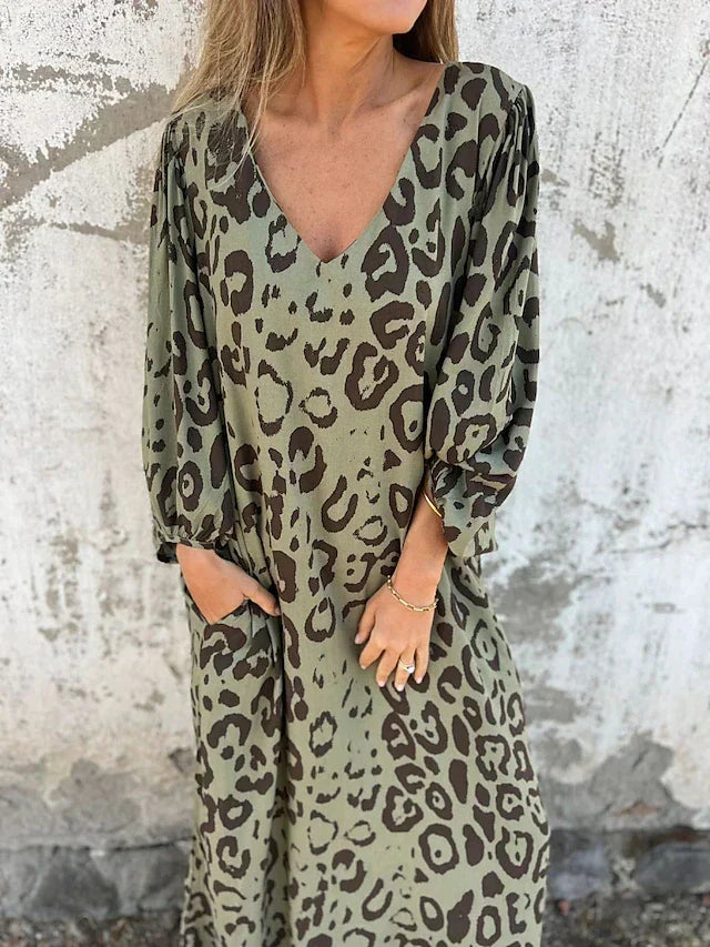 Woman in the Alison leopard print maxi dress with long sleeves and a V-neckline, walking along the shoreline.